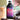 A 32-ounce bottle of Rook Coffee’s Coconut Mocha Style cold brew concentrate stands upright on a wooden surface. To the left is a glass of iced cold brew with condensation, and to the right are chocolate pieces, a halved coconut filled with chocolate chunks, and green plant leaves blurred in the background. The bottle’s label is purple and magenta with white text reading “coconut mocha style – limited release cold brew concentrate,” topped with the Rook Coffee logo.