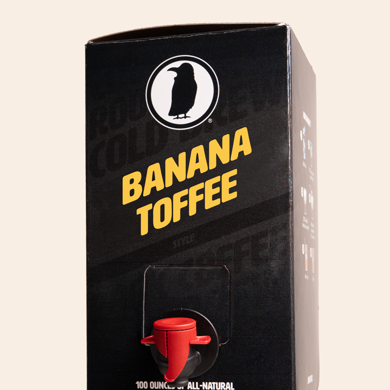 Black Rook Coffee box labeled ‘Banana Toffee’ with yellow text and the Rook Coffee logo at the top. The front features a red dispensing spout near the bottom and indicates 100-ounces of all-natural cold brew.