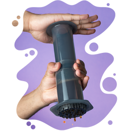 Two hands pressing down on an AeroPress coffee maker as fresh coffee drips from the bottom, set against a purple background with abstract shapes.