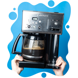 Two hands holding up a drip coffee maker filled with freshly brewed coffee, set against a bright blue background with abstract shapes.