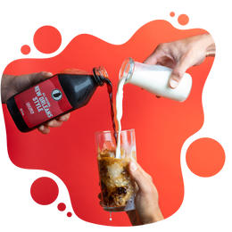 Hands pouring cold brew coffee and milk into a glass filled with ice against a red background.






