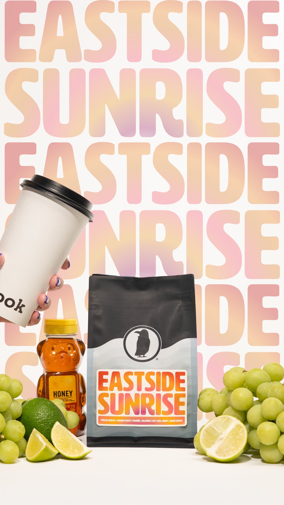 Bag of Eastside Sunrise coffee with honey, limes, green grapes, and a hand holding a Rook Coffee cup in front of colorful background.
