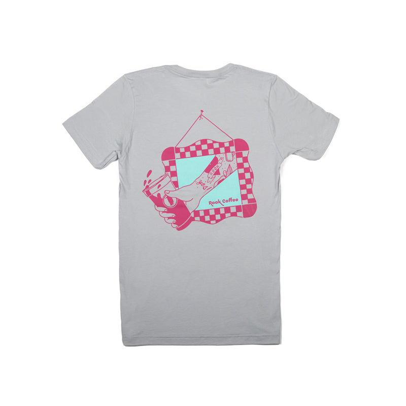 Gray tee shirt with a design of a pink hand holding a cold brew cup coming through a frame on a light blue background.