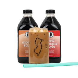 Two Rook Coffee cold brew bottles behind a glass of cold brew with a mint green straw.