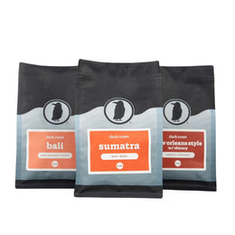 Three Rook Coffee dark roast bags labeled Bali, Sumatra, and New Orleans Style arranged in a row.