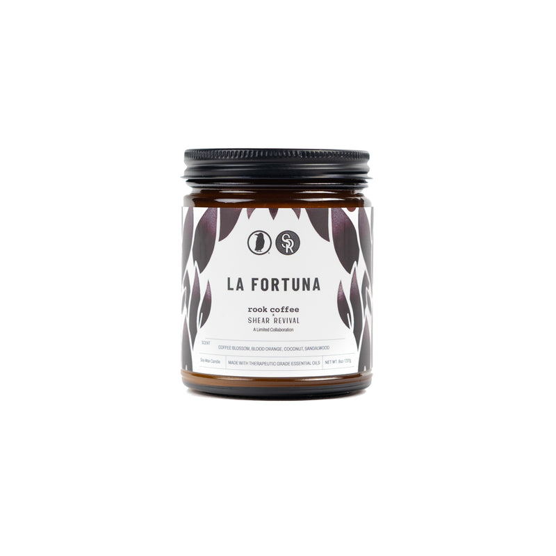 A short candle labeled 'La Fortuna rook coffee x shear revival a limited collaboration, coffee blossom, blood orange, coconut, sandalwood,'
